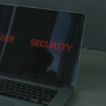 The image shows a laptop screen displaying the words "Cyber Security", suggesting a focus on computer security and protection against digital threats.
