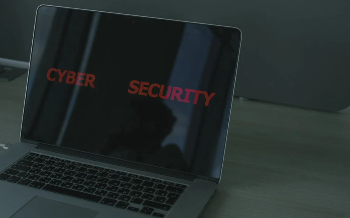 The image shows a laptop screen displaying the words "Cyber Security", suggesting a focus on computer security and protection against digital threats.