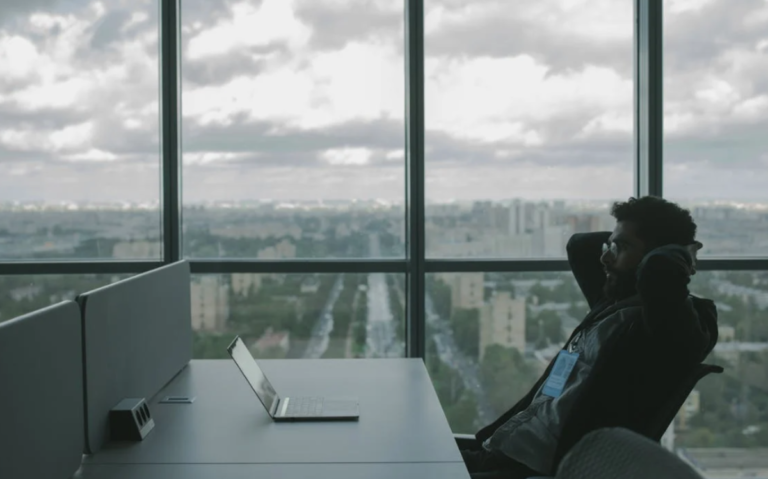 A person is seen in a workspace with a cityscape visible through the window, creating a serene and reflective setting for their work or activities.