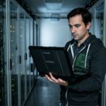 Engineer checking a laptop in a server room while ensuring log data integrity transport systems run smoothly